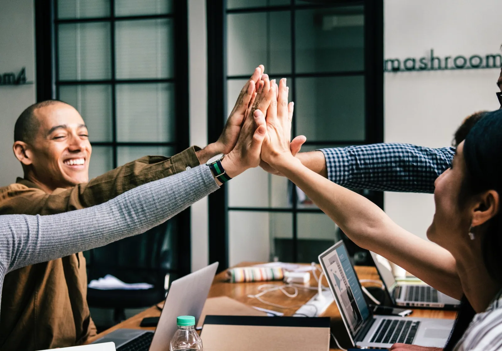 Group of coworkers giving a high-five over an office table with laptops