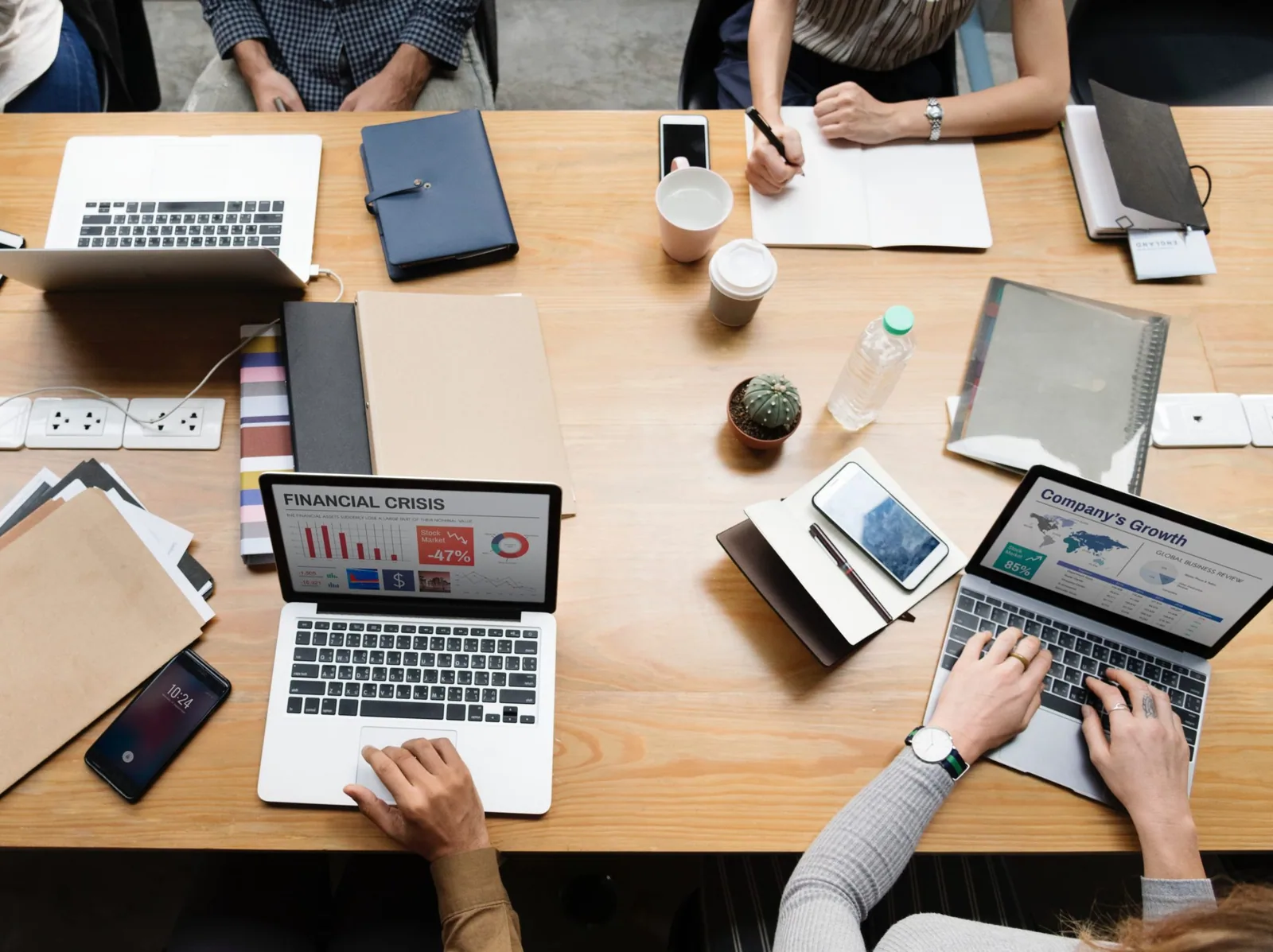 Overhead view of coworkers at a wooden table with laptops showing financial charts