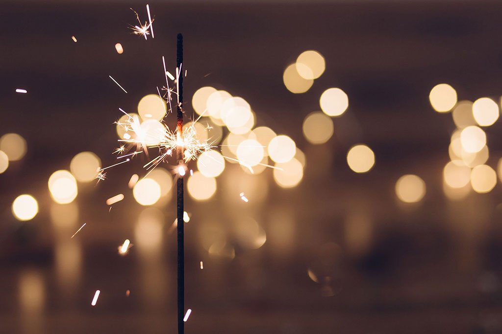 Lit sparkler emitting bright sparks against a bokeh light background