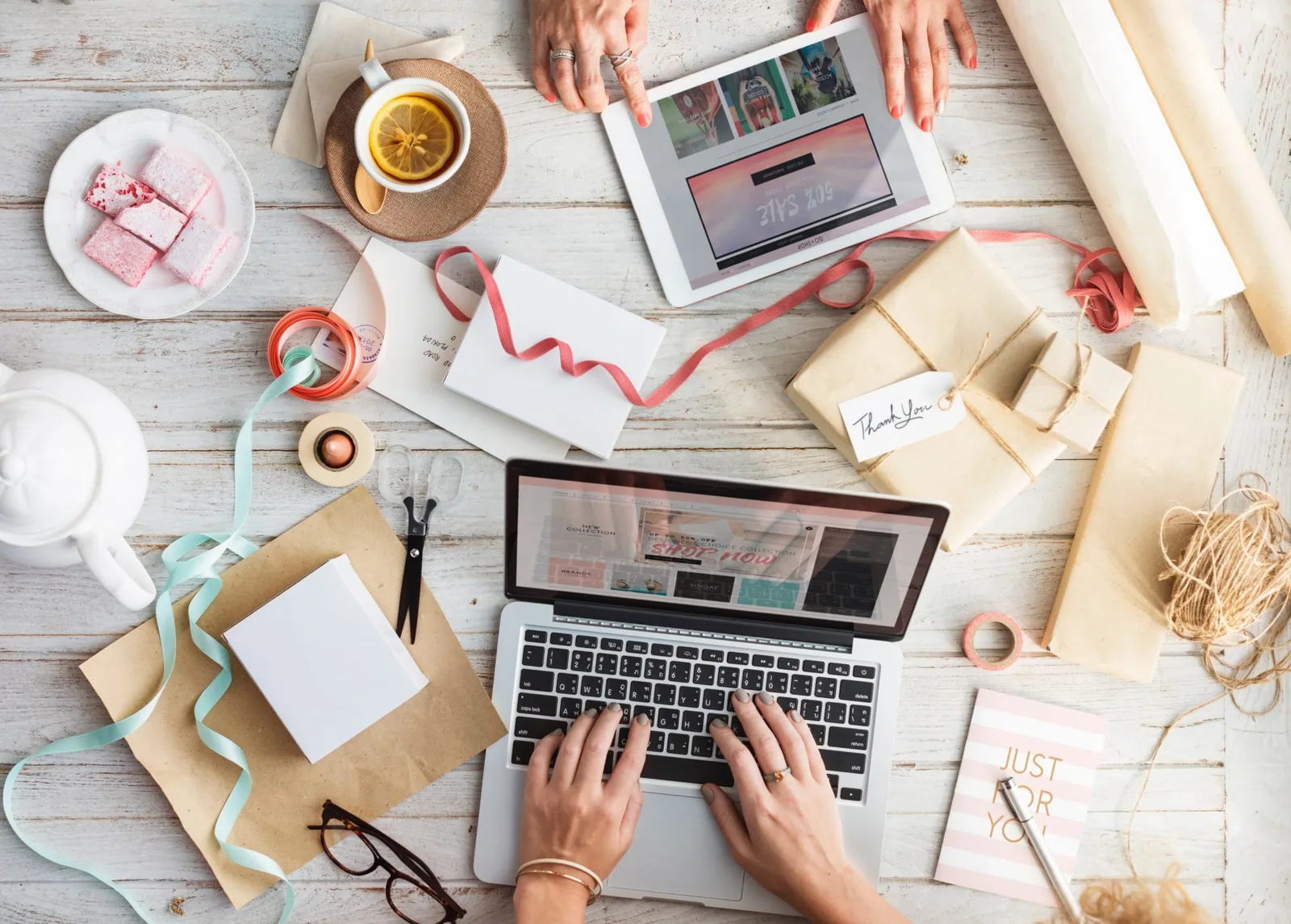 Overhead view of two people on laptops surrounded by gift wrap, ribbons, and tea