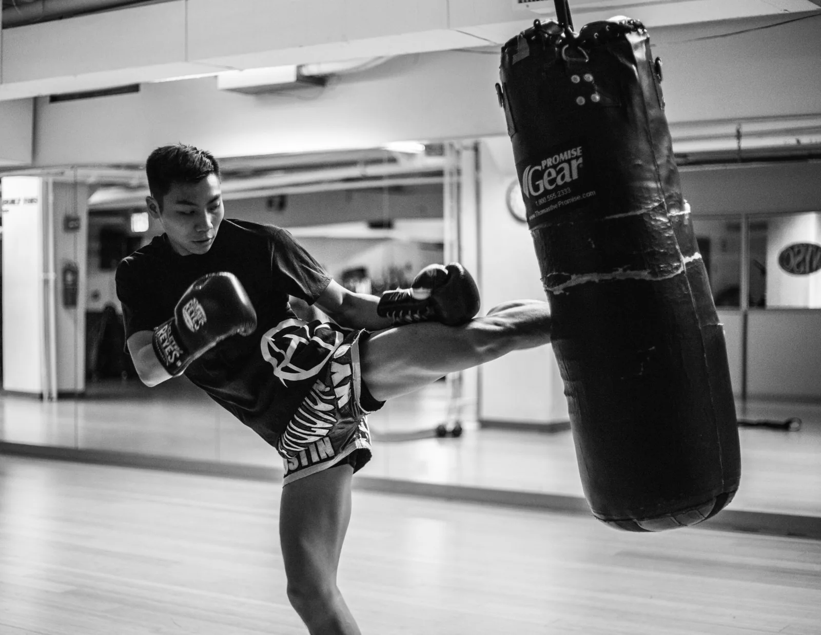 Black and white photo of a man kickboxing a heavy bag in a gym