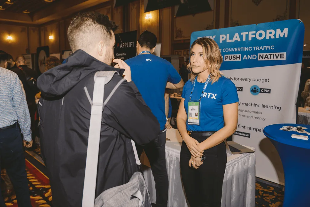 Woman in blue shirt speaking with attendees at a marketing trade show booth