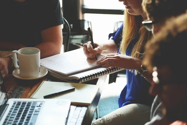 Group of coworkers sitting at a cafe table with notebooks, coffee cups and a laptop