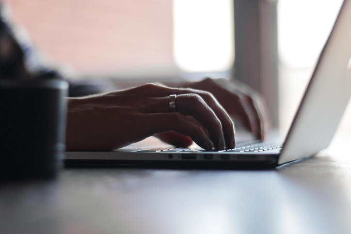 Close-up of hands typing on a silver laptop keyboard with soft window light