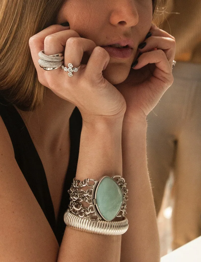 Woman wearing silver rings and a turquoise stone bracelet, hands resting near her face.