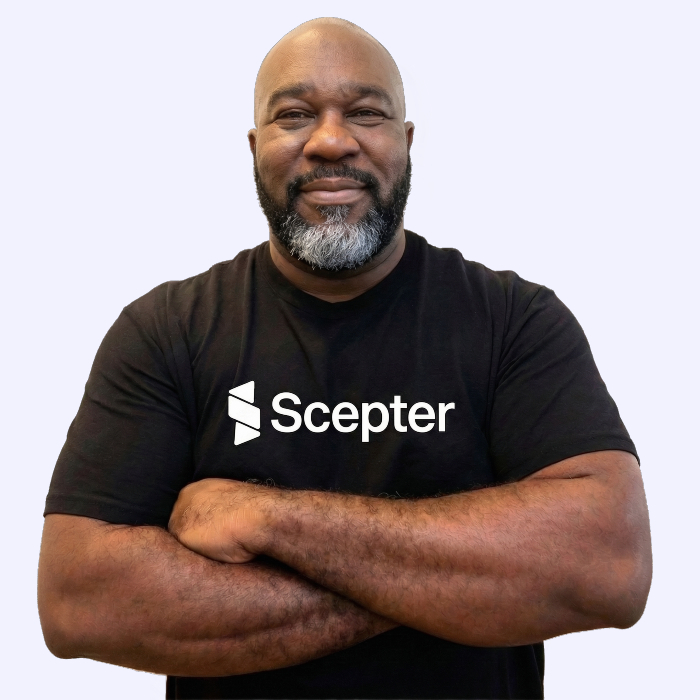 Bald bearded man in a black Scepter t-shirt smiling with arms crossed